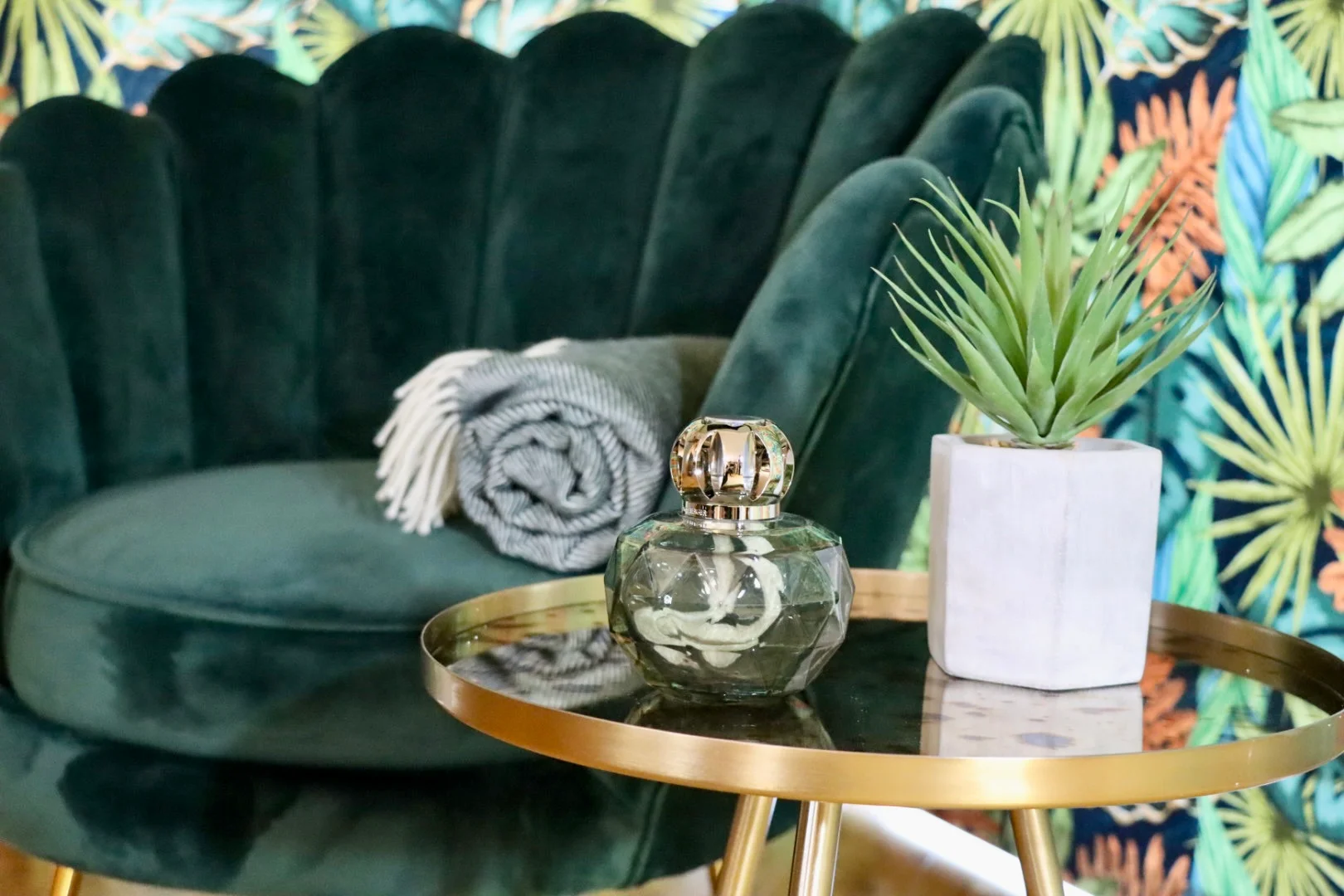 Home fragrance and faux plant on gold side table with green chair in background