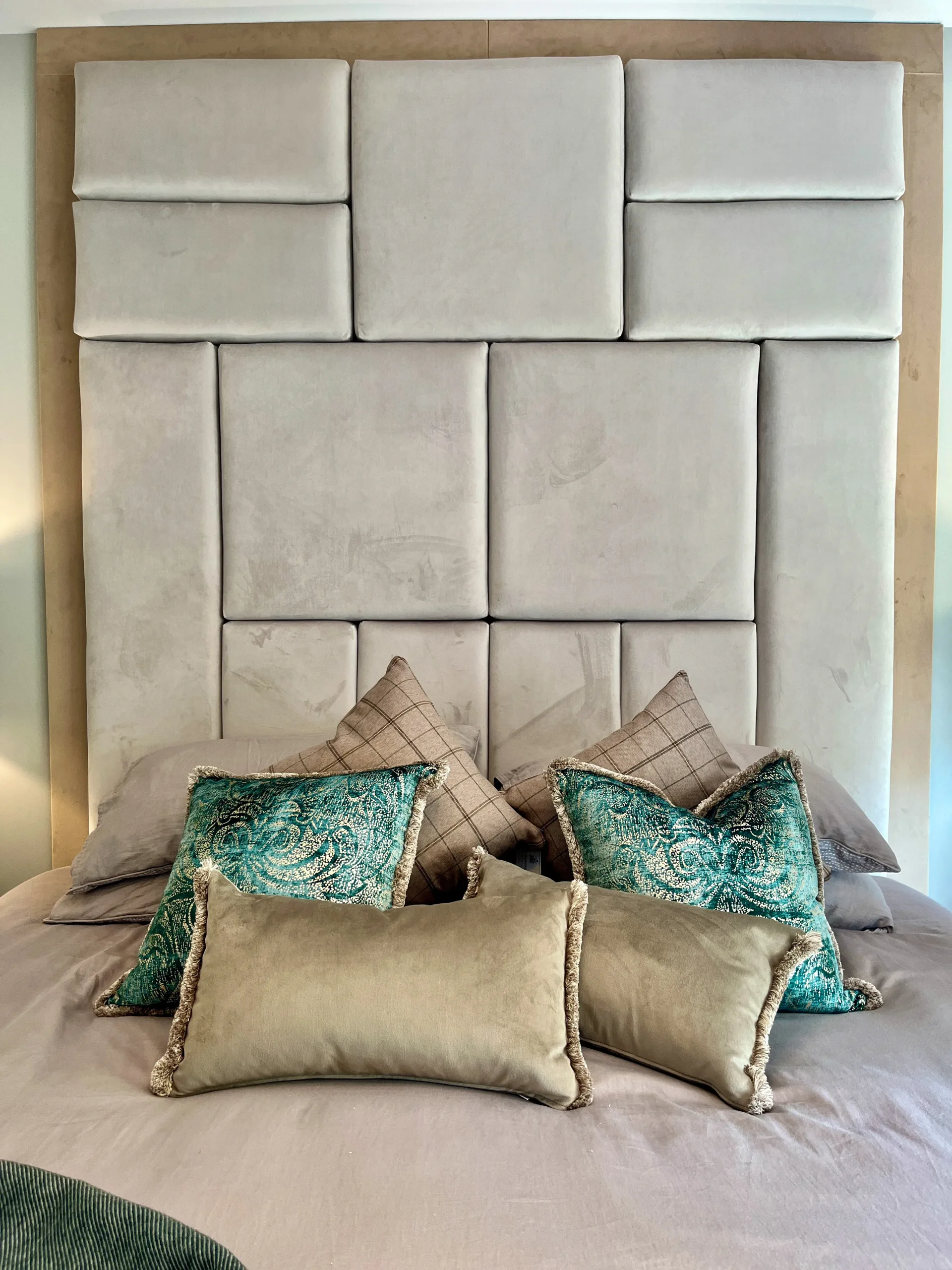 Large suede effect neutral headboard with cushions on bed in neutral and green tones.